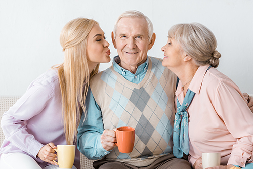 Grandfather sitting between his granddaughter and wife both blowing him kisses