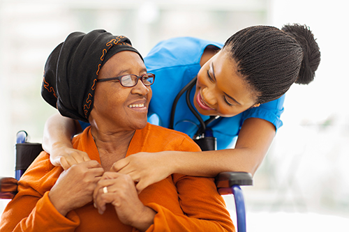 CNA with her arms around the shoulders of elderly woman in wheelchair